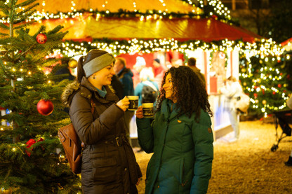 Zwei junge Frauen stoßen mit Punsch an auf dem Kieler Weihnachtsmarkt