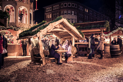 Zwei junge Frauen sitzen überdacht an einem Tisch auf dem Kieler Weihnachtsmarkt auf dem Asmus-Bremer-Platz