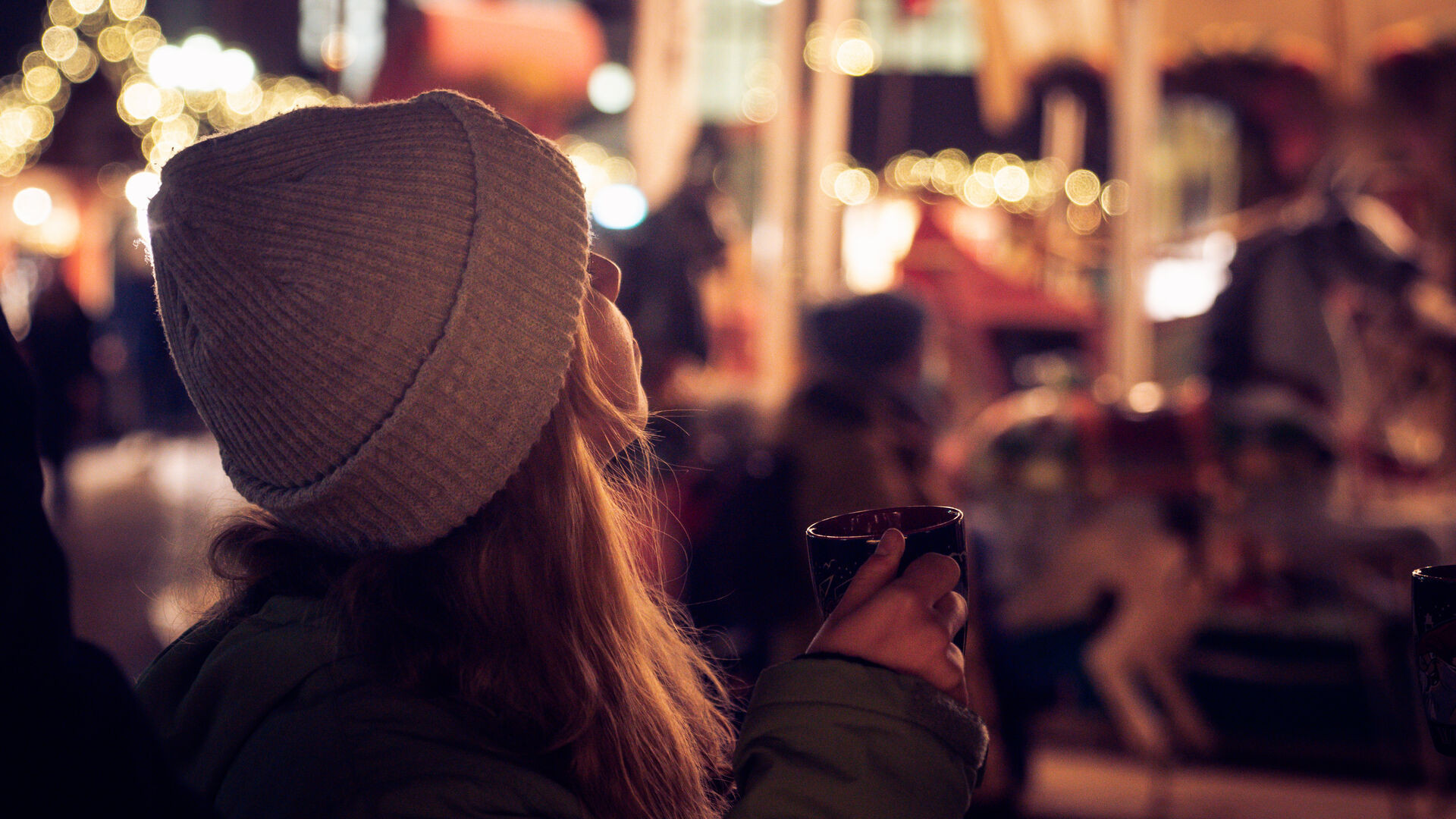 Frau hält Glühweintasse in der Hand und guckt in die Ferne 