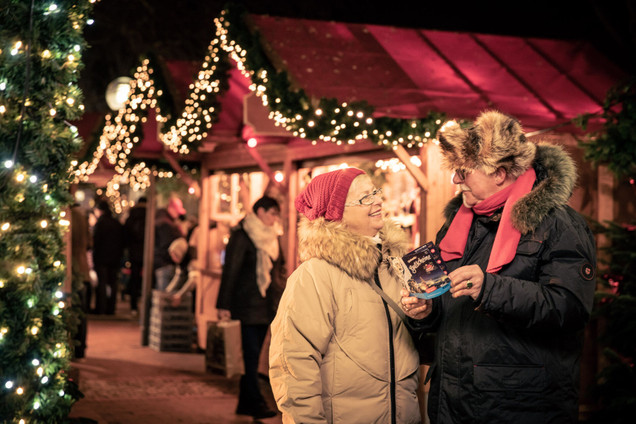 Älteres lächelndes Pärchen mit dem Gutscheinheft auf dem Weihnachtsmarkt