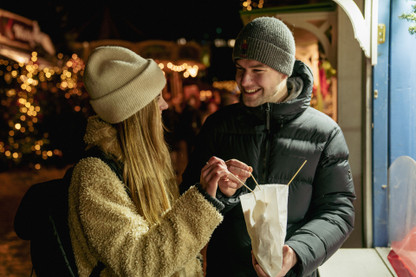 Ein junges Paar teilt sich eine Tüte Muzen auf dem Weihnachtsmarkt