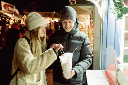 Junges Pärchen isst Schmalzgebäck auf dem Weihnachtsmarkt