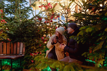 Ein junges Paar sitzt mit je einer Tasse Glühwein in der Hand in winterliche Atmosphäre auf der Bank eines Weihnachtsmarkts