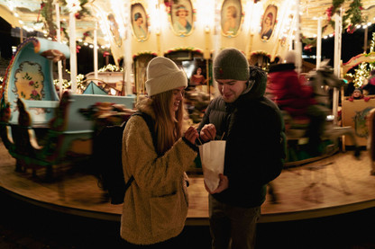Ein junges Paar teilt sich eine Tüte Muzen auf dem Weihnachtsmarkt